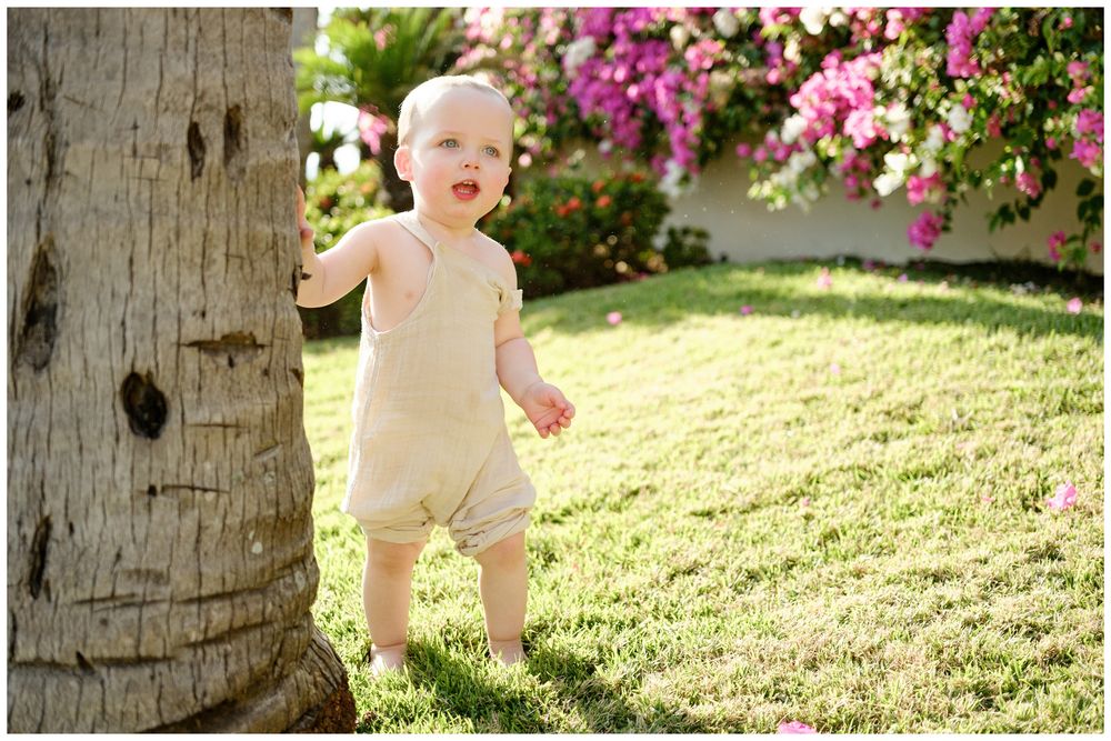 Grand Velas Riviera Nayarit Family Photographer capturing a baby standing near palms and flowers during candid family photos.