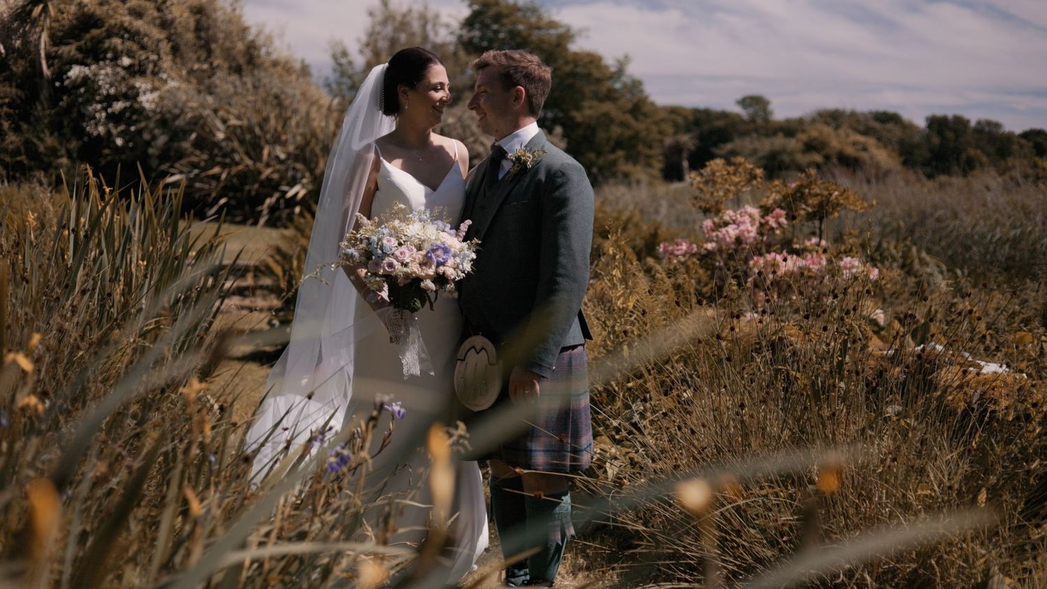 Bride and groom smiling at each other in Whithorn, Dumfries and Galloway amidst golden greenery