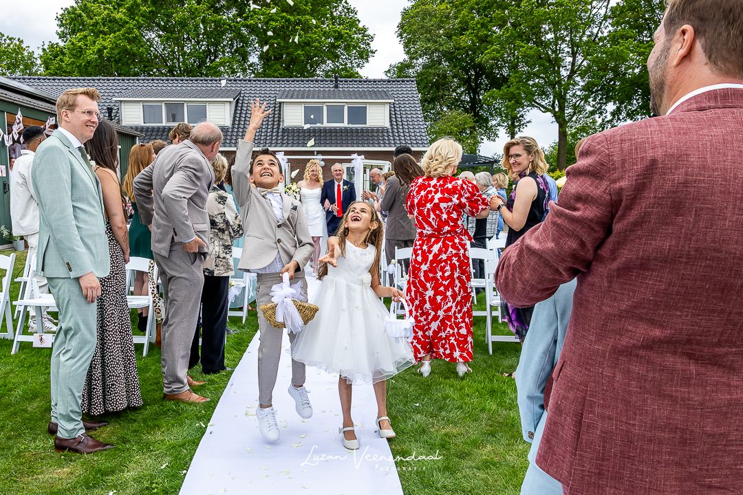 Bruidskinderen lopen over de loper en strooien bloemblaadjes, vlak voordat de bruid met haar vader arriveert