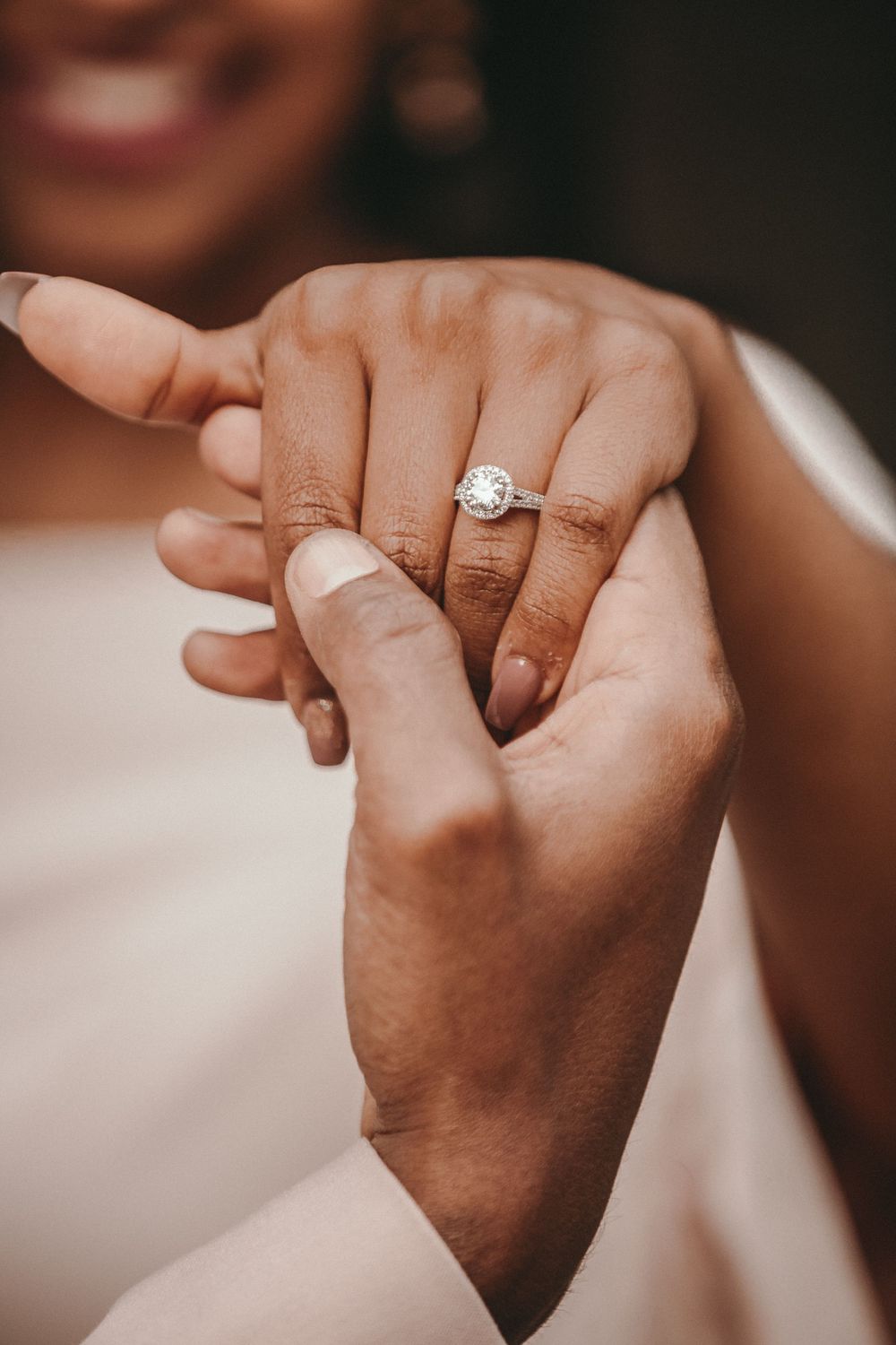 Close-up of a couple holding hands displaying a elegant round diamond halo engagement ring on the bride's finger.