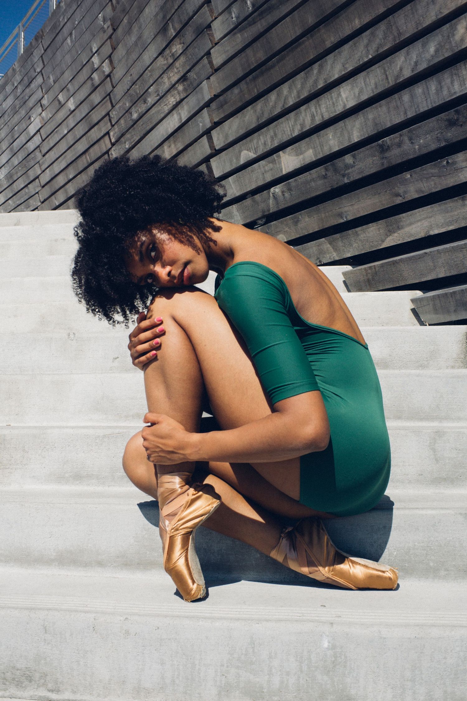 Seattle Dancer in green leotard curled into a seated pose on stone steps, soft golden light during ballet photoshoot