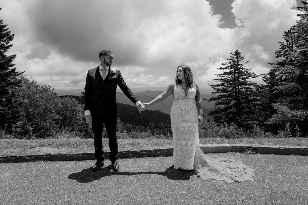 Black and white photo of bride and groom holding hands with mountain scenery.