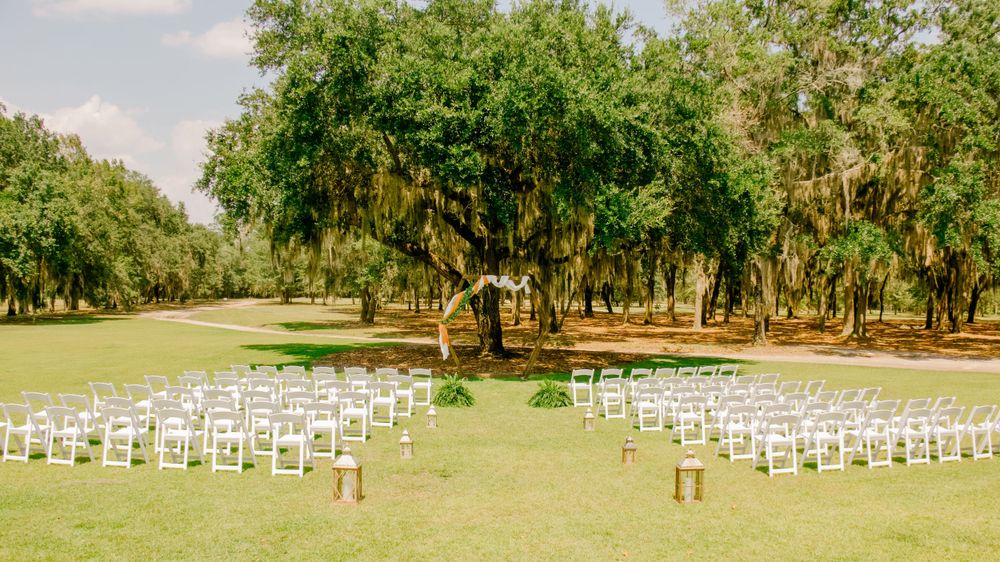 White wedding ceremony chairs arranged in rows on a green lawn with Spanish moss trees.