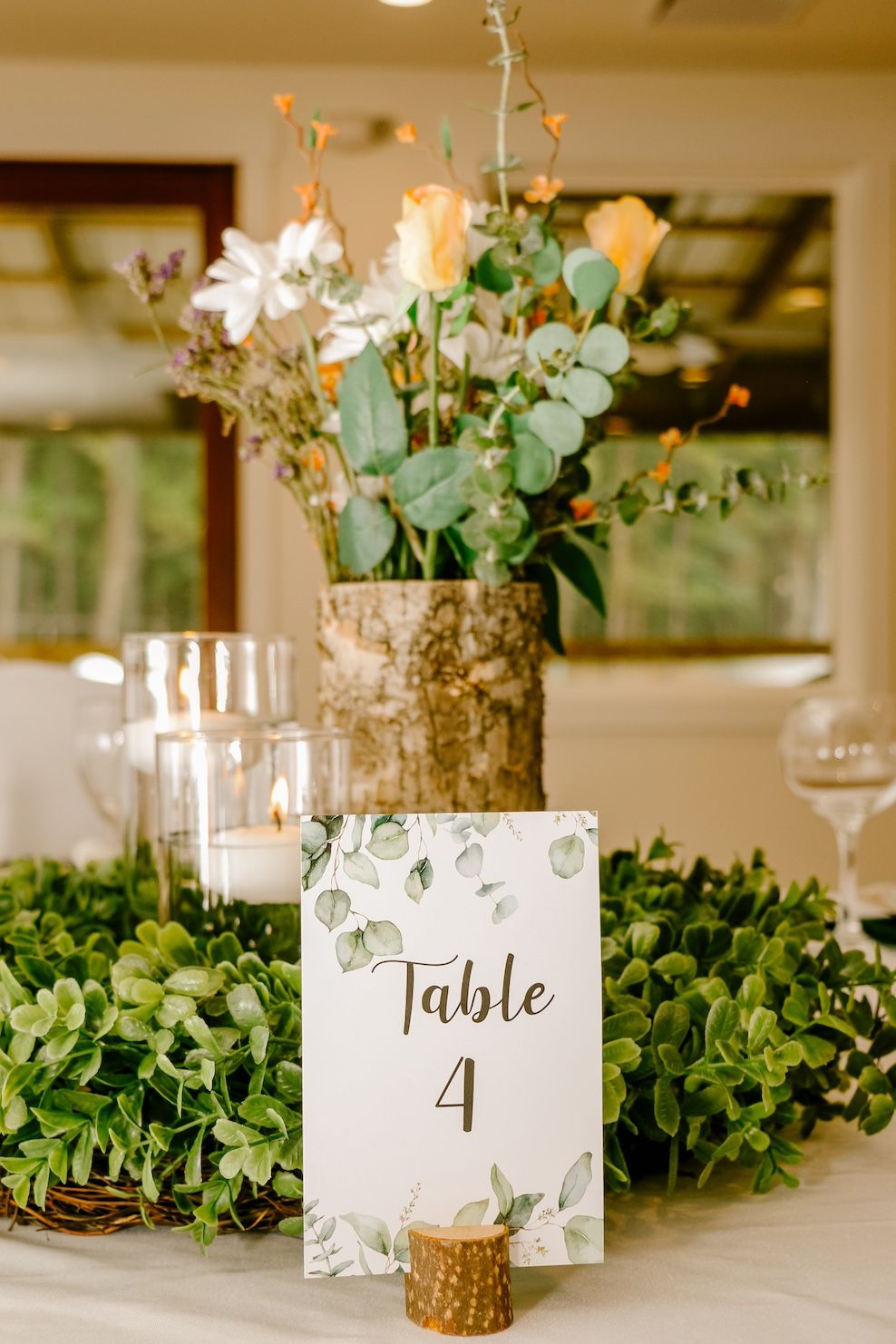 Elegant wedding table centerpiece with birch bark vase, eucalyptus, roses and table number 4 card.