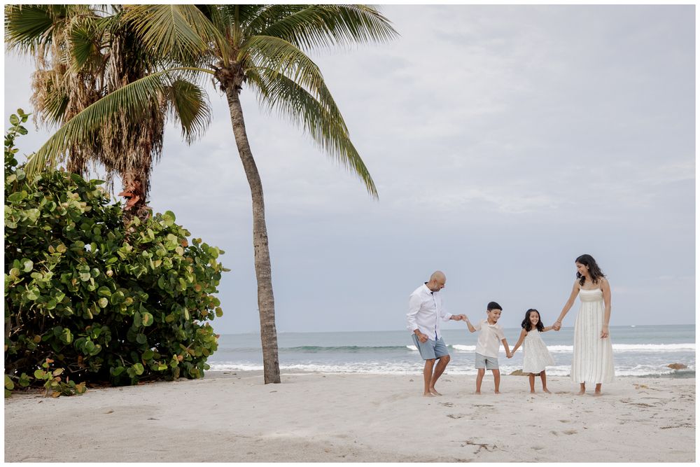 St Regis Punta Mita Family Photographer capturing a family playing by the ocean beneath a palm tree during Beach Family Photo Session.