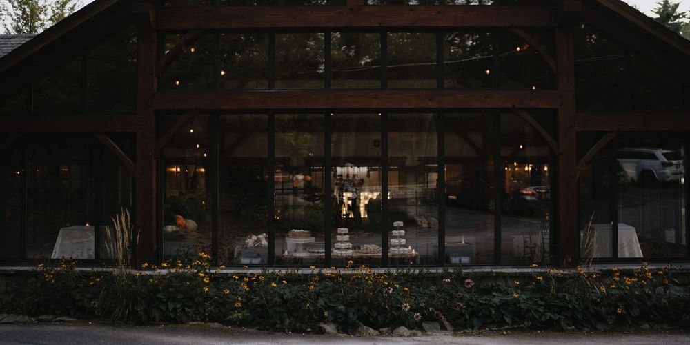 Elegant rustic wedding venue with large glass windows and warm interior lighting at dusk.