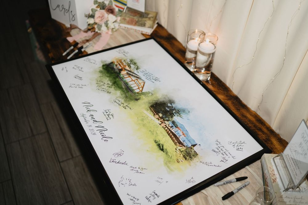 Watercolor wedding venue guest book print with signatures displayed on rustic wooden table with candles.