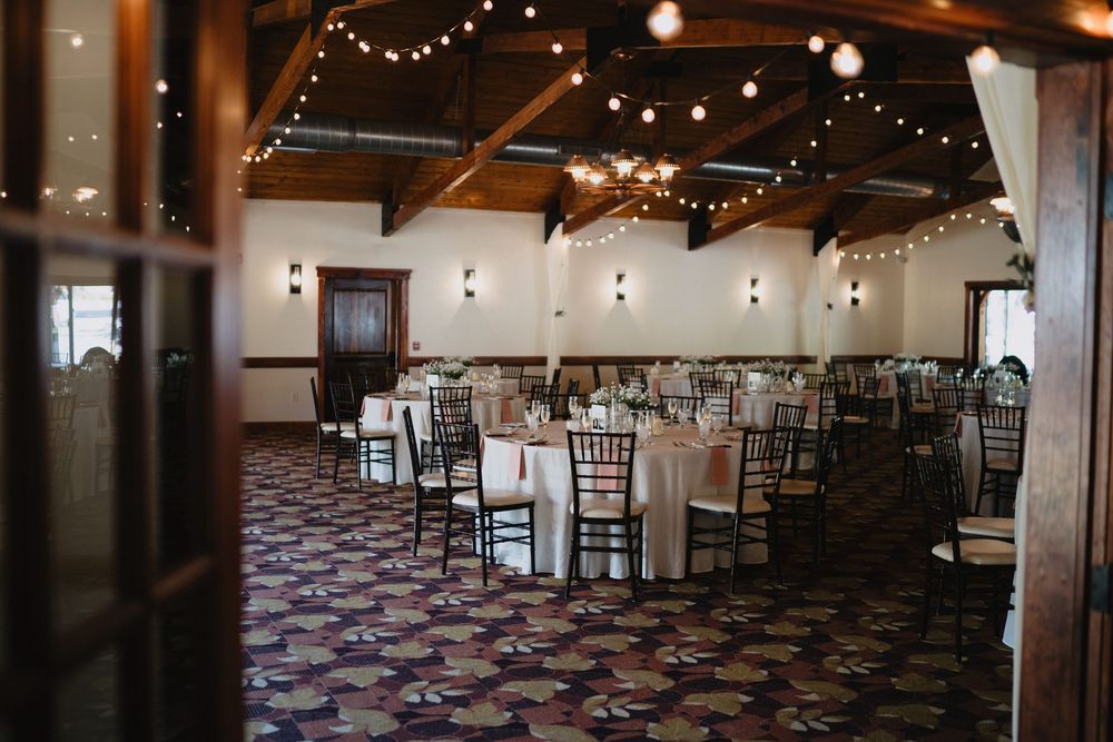 Elegant wedding reception hall with round tables, chiavari chairs, string lights, and patterned carpet.