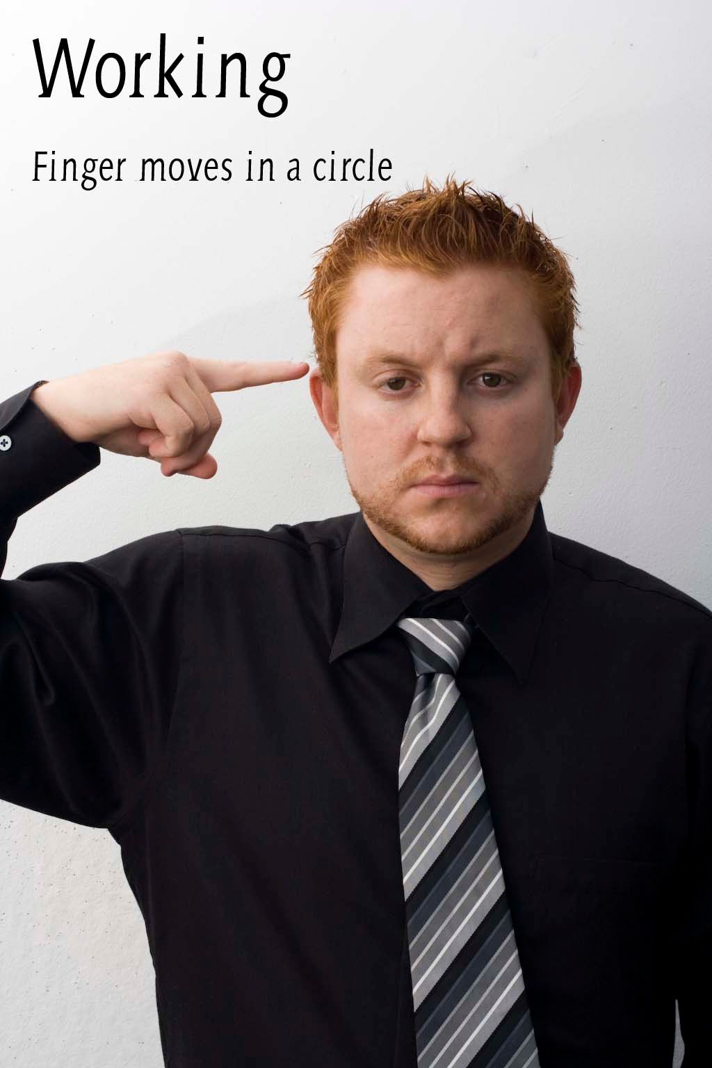 Man in black shirt and tie pointing finger to temple demonstrating working sign language gesture.