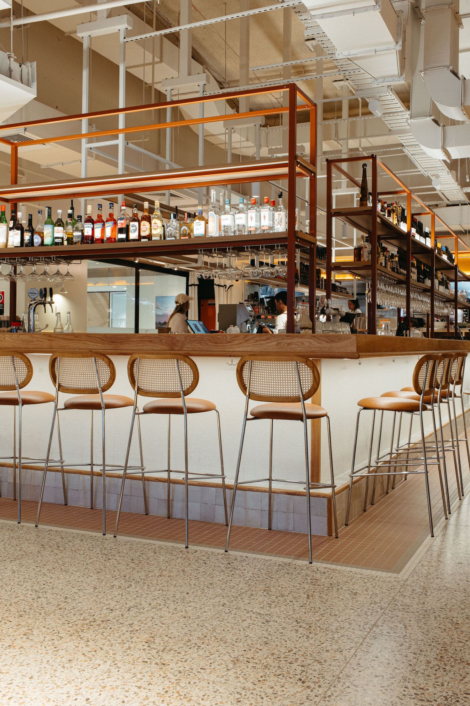 Modern bar with leather stools, copper shelving, bottled spirits, and terrazzo floors in a stylish restaurant.