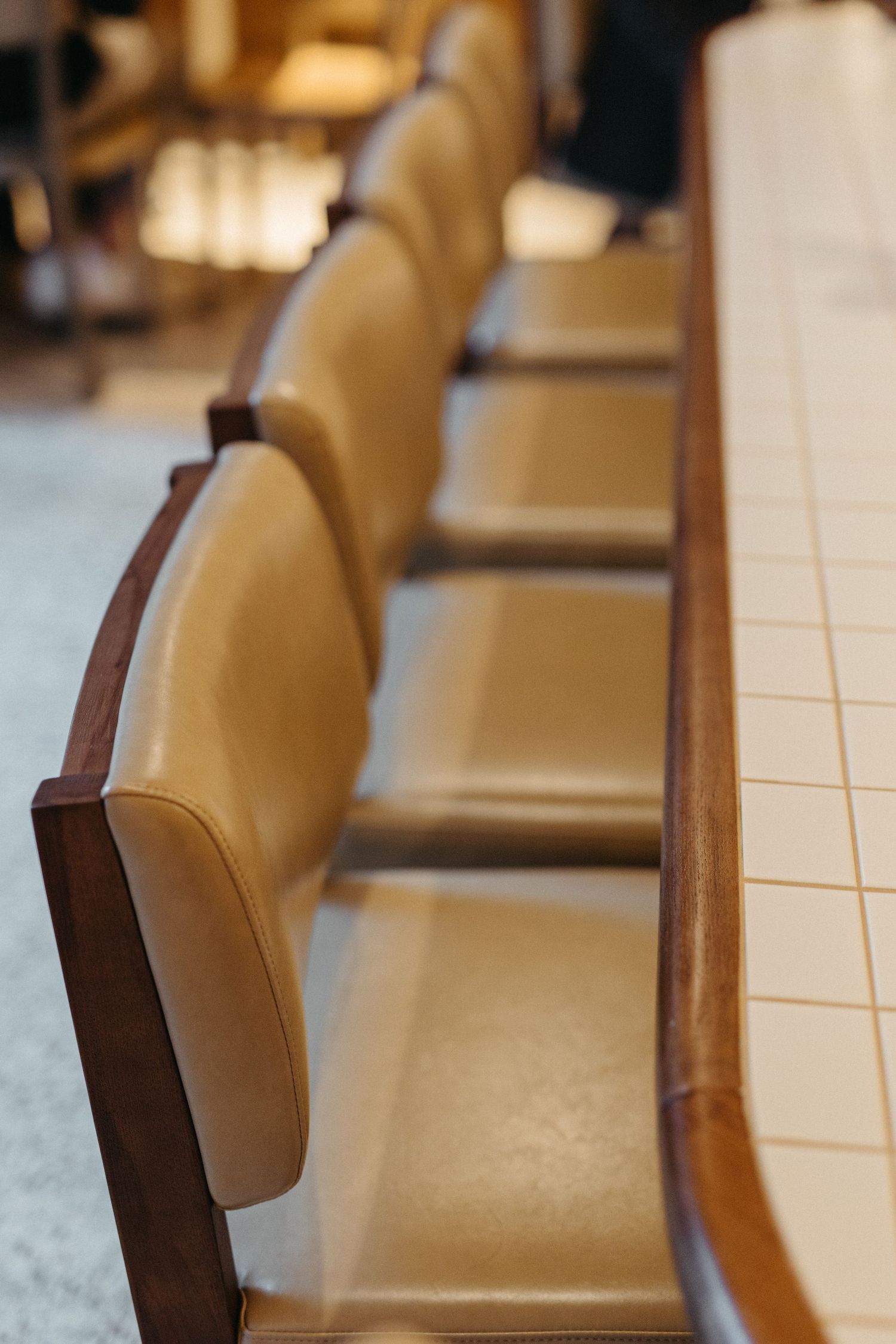 Row of tan leather chairs with wooden frames lined up along a tiled counter in a retro-style diner.