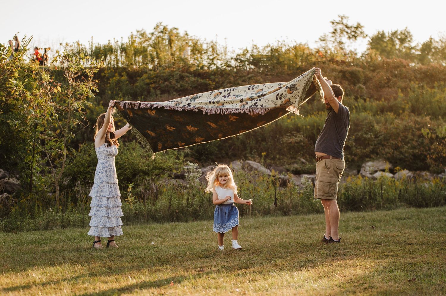 A happy family plays with a lace blanket in a sunny green field at golden hour.