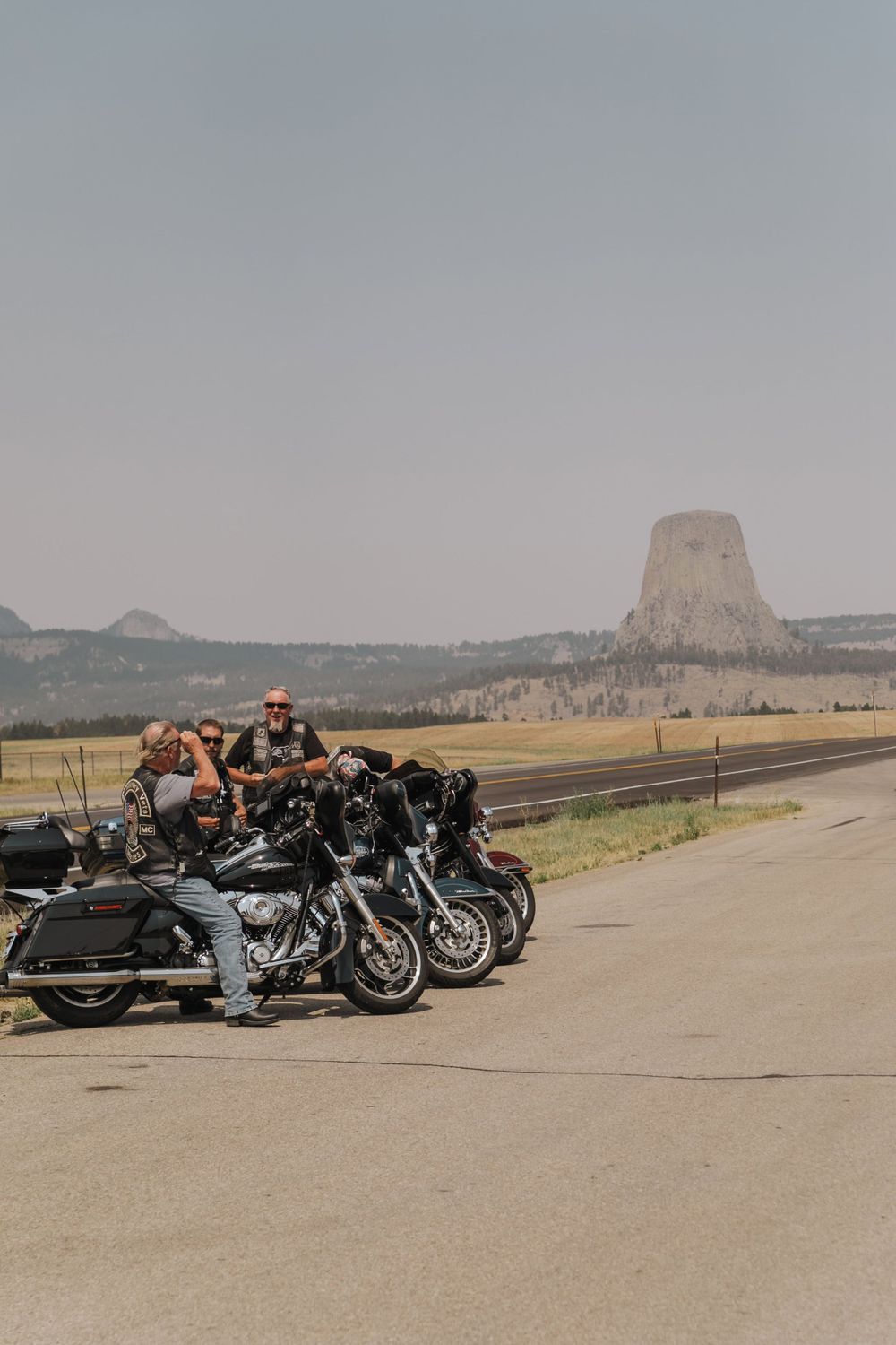 A row of parked motorcycles on a road with Devils Tower National Monument visible in the background landscape.