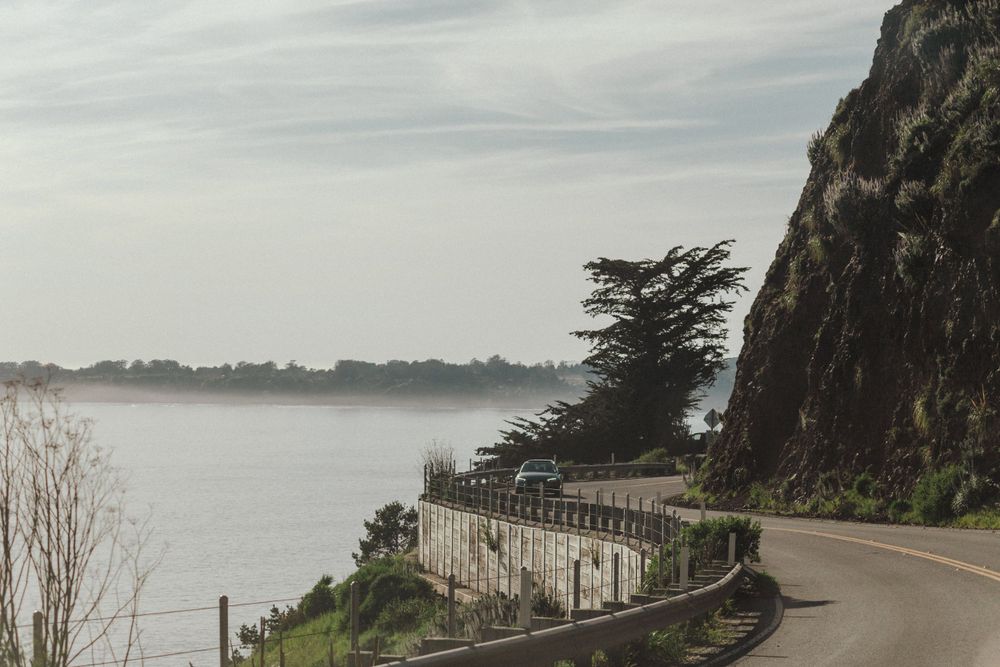 Scenic coastal road winding along cliffs with guardrails and misty ocean views.