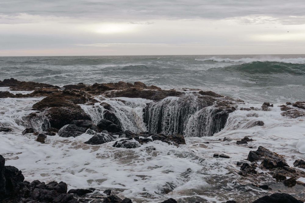 Ocean waves crash and cascade over dark rocky formations at Thor's Well, a natural sinkhole on the Oregon Coast.