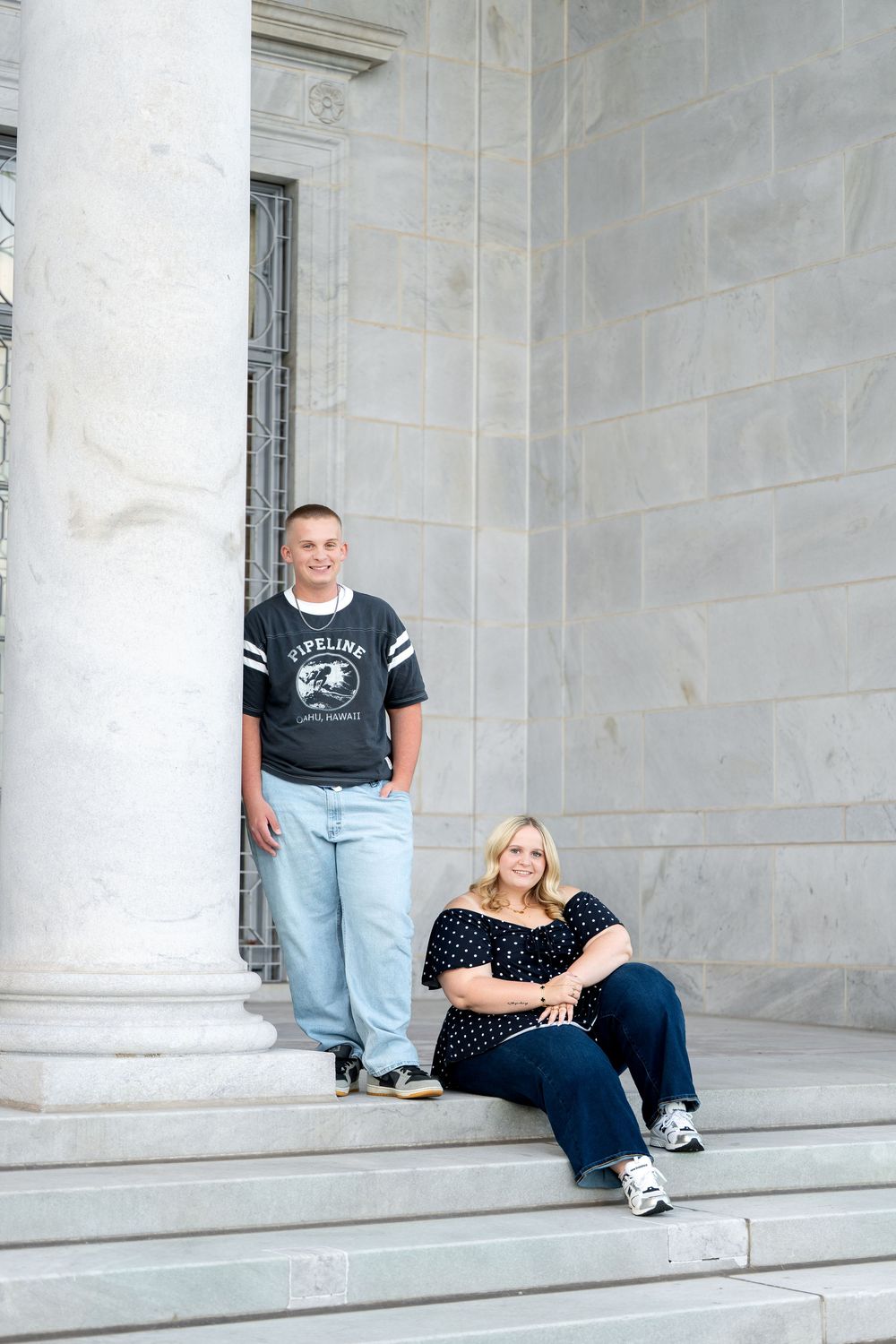 A young man and woman pose on marble steps near columns for a portrait photo session.
