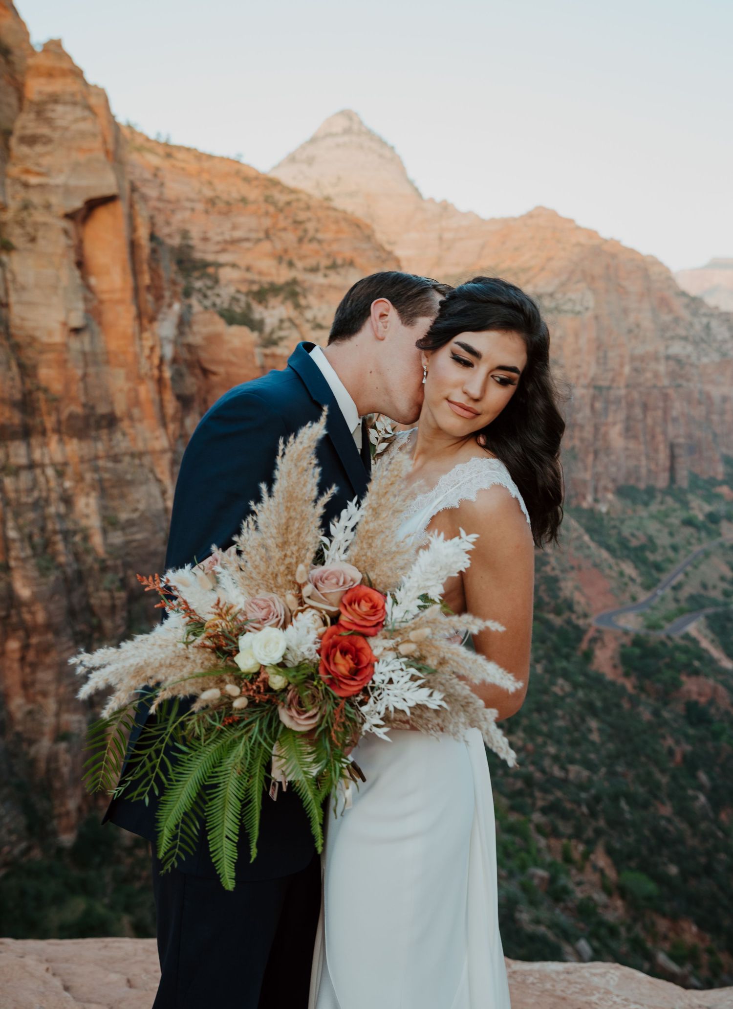 Bride and groom share a romantic kiss on a rocky overlook at Zion National Park with stunning canyon views.