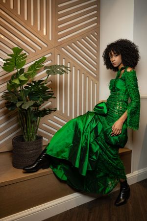 Emerald green sequined gown styled against geometric wooden wall panels with tropical plants.