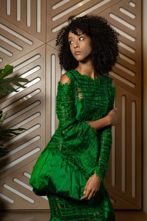 Elegant emerald dress with ruched details showcased against modern geometric wall design.