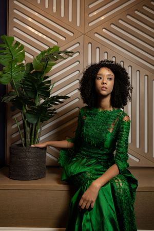 Emerald green couture dress displayed in artistic poses against geometric wall backdrop.