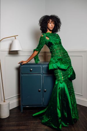 Luxurious green evening gown photographed against navy cabinet in minimalist setting.