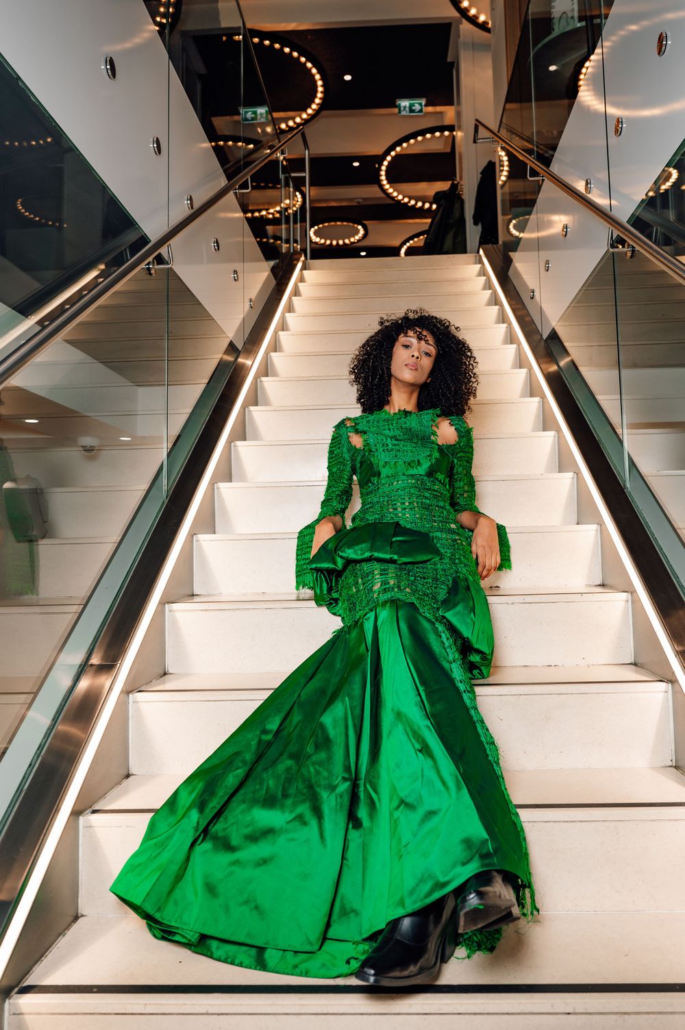 Dramatic emerald ball gown captured on white staircase with overhead lighting.
