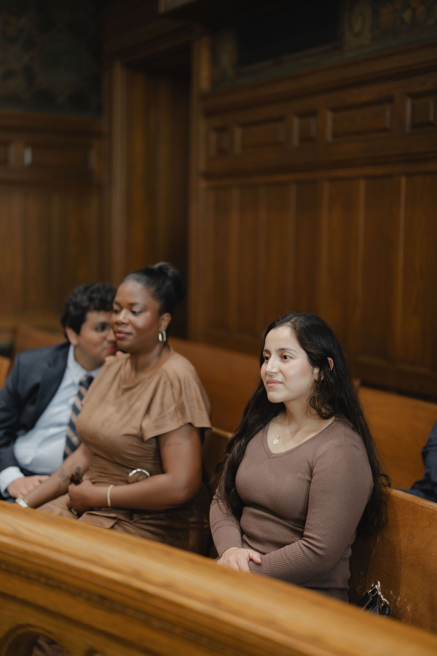 Diverse wedding guests seated in wooden church pews, smiling and watching a ceremony.