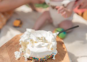 Baby's first birthday cake smash with white frosted cake, rainbow sprinkles, and gold number one candle on wooden board.