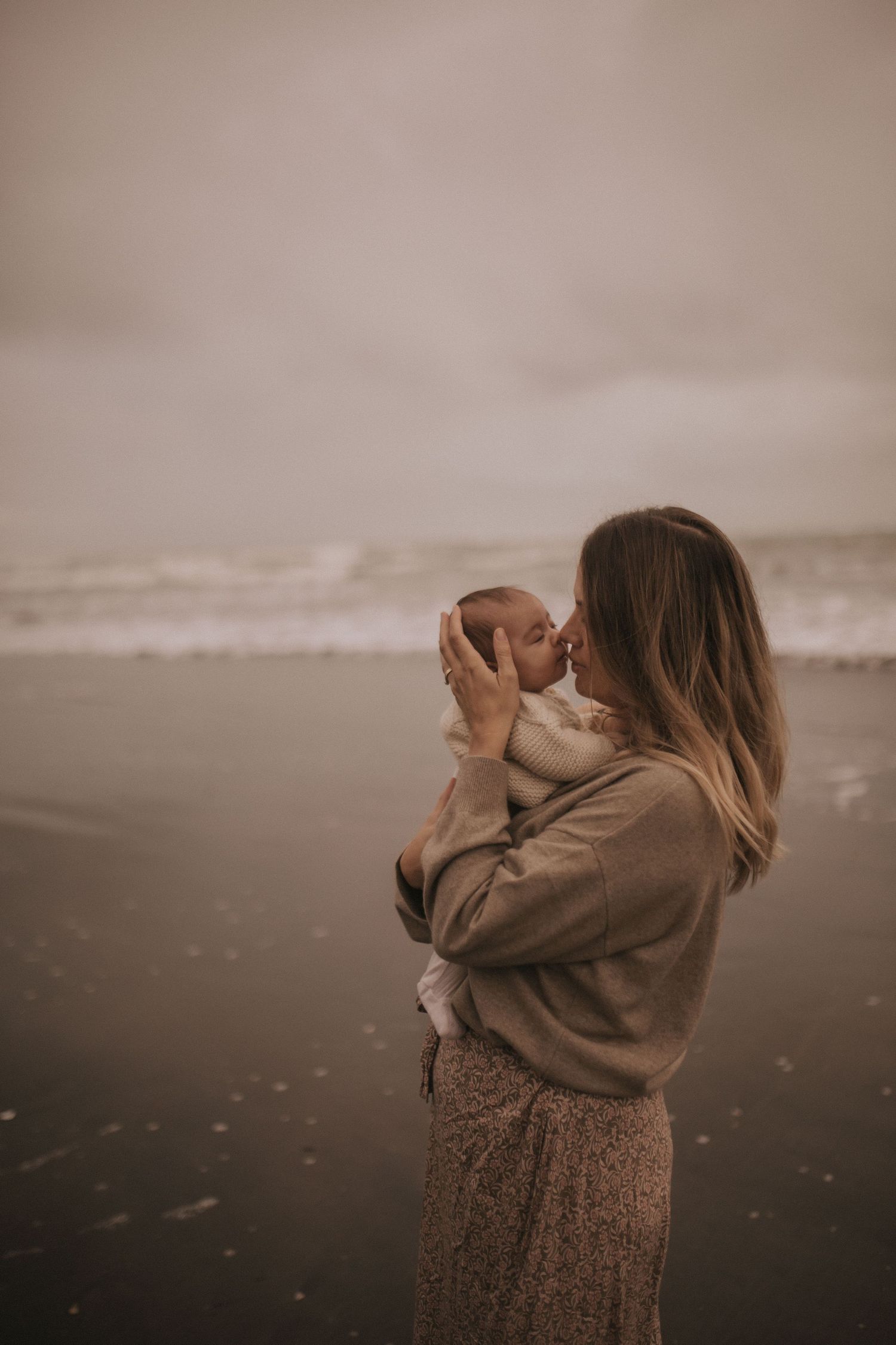 Mother gently kissing new born baby during a motherhood portrait session with Nami Creative in Raglan, New Zealand.