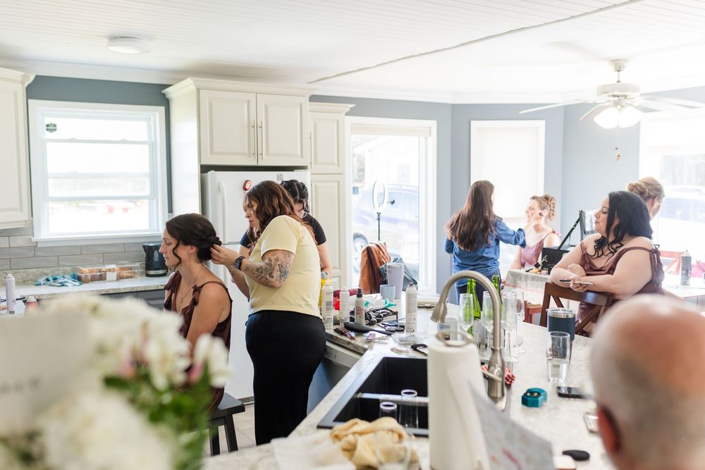 Women gathered in a bright kitchen with white cabinets and blue walls, socializing and preparing food together.