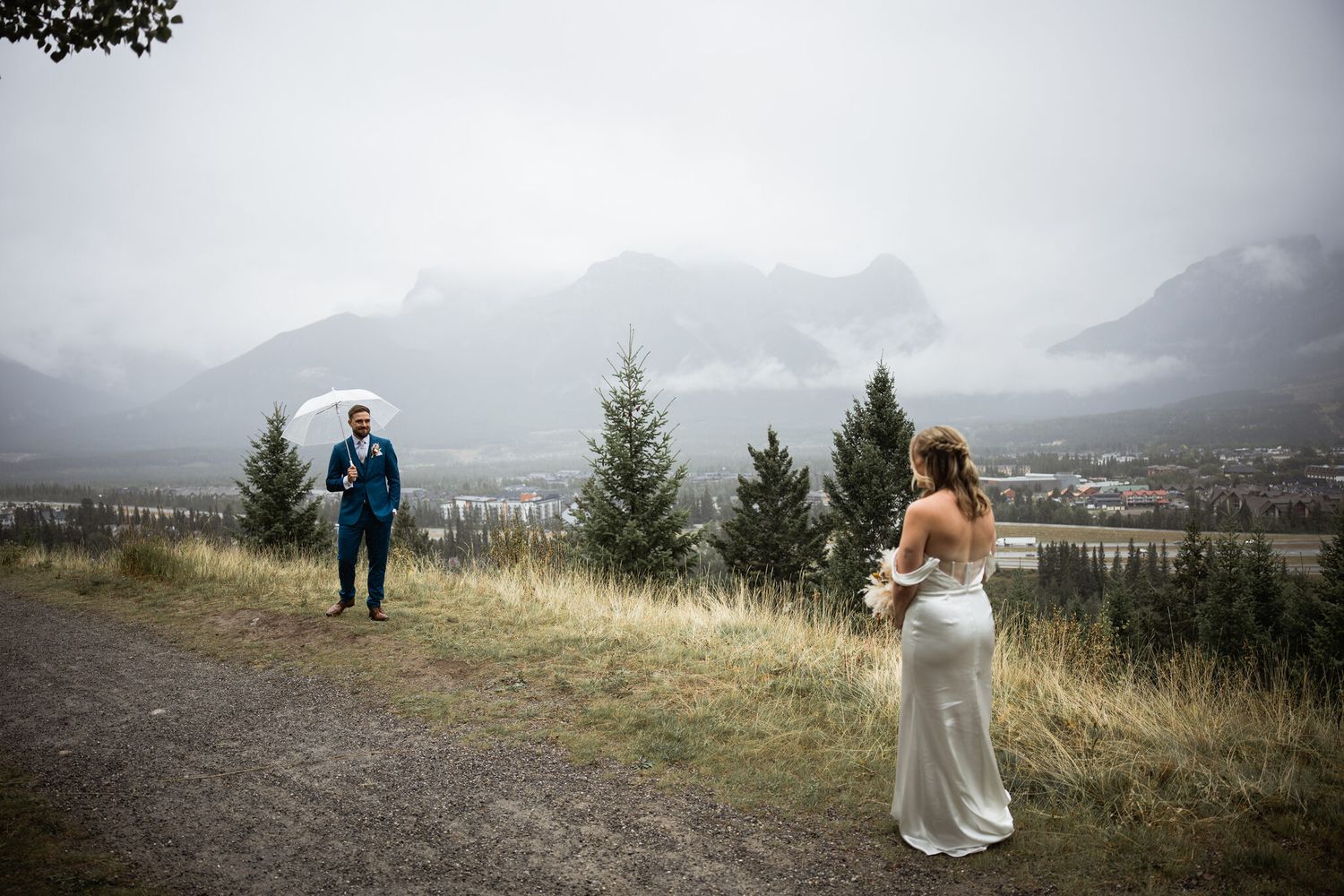 Bride walking toward groom for first look among evergreens at Vista in Canmore