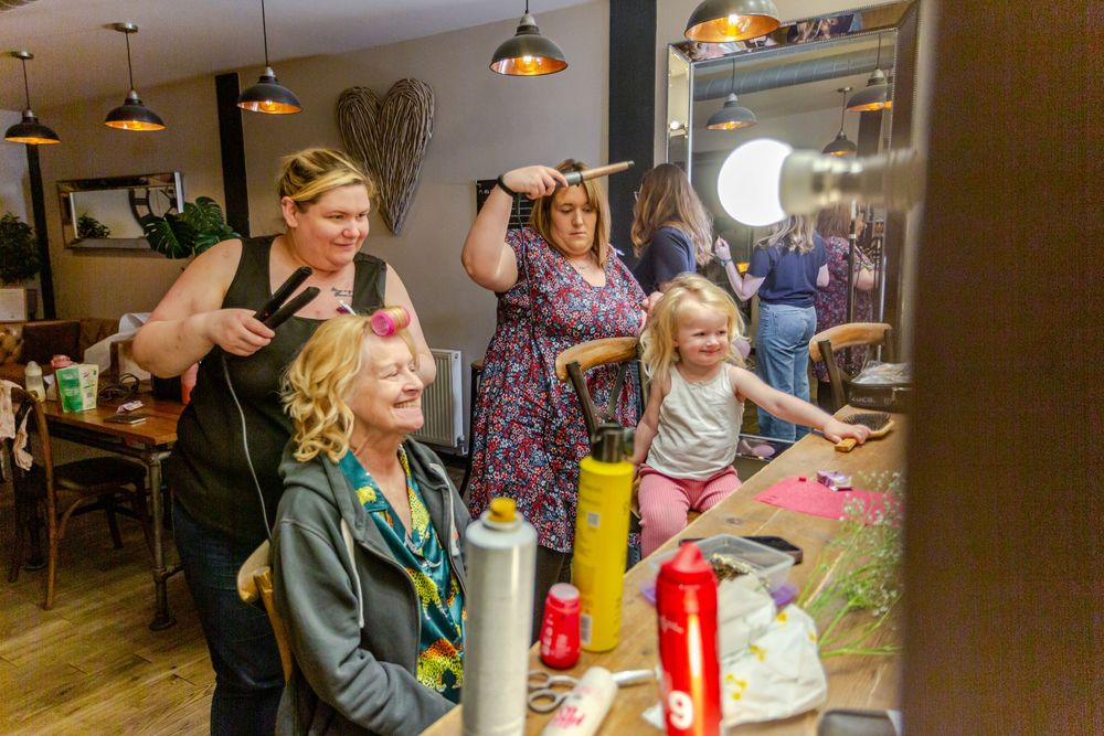 Women and child gather around a salon chair during a hair styling session in a cozy restaurant setting.