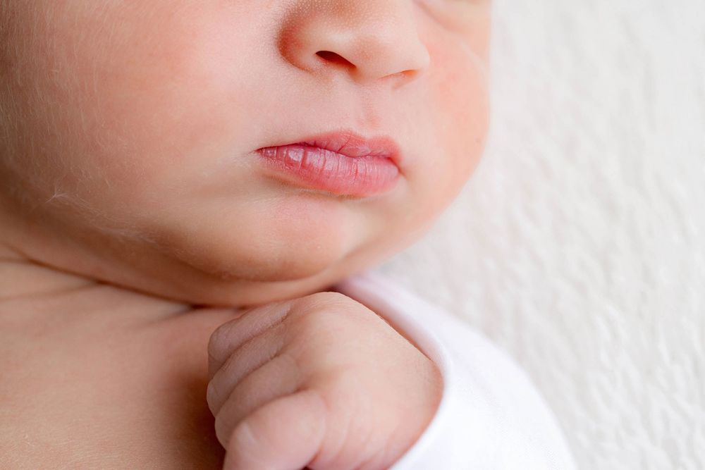 Close-up of a peaceful newborn baby's face and tiny hand in white wrap.