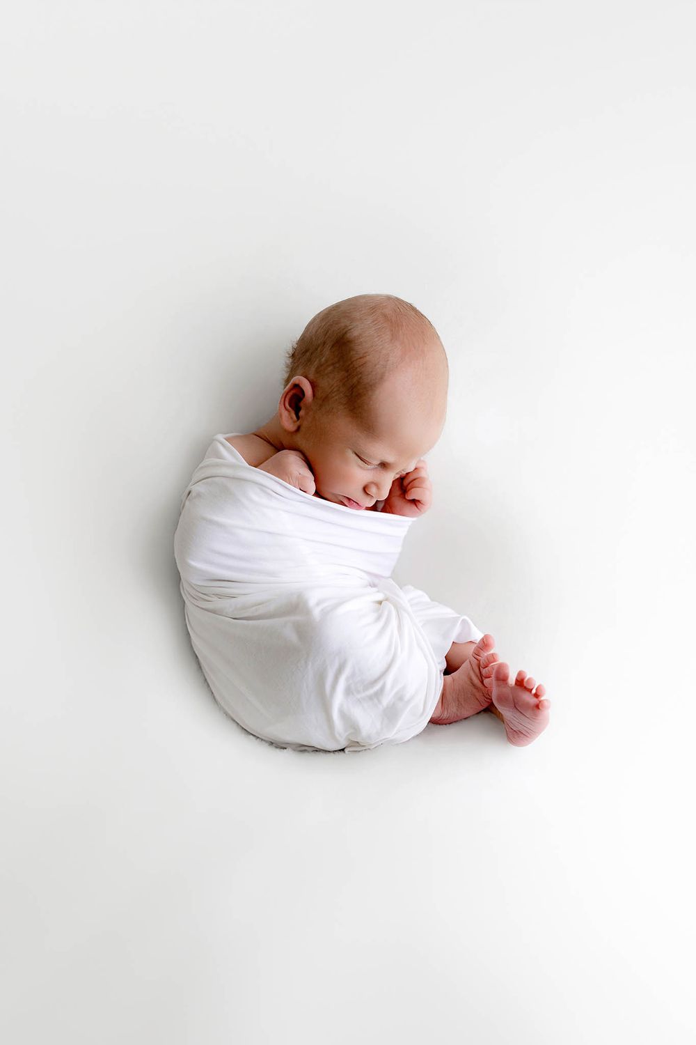 Peaceful newborn baby swaddled in white wrap sleeping on white background.