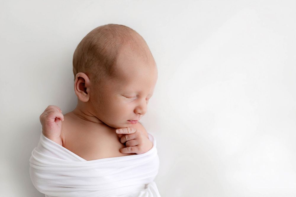 Peaceful newborn baby swaddled in white wrap sleeping on white background.