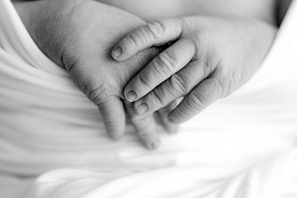 Black and white close-up of a newborn baby's tiny hand resting gently on an adult's hand.
