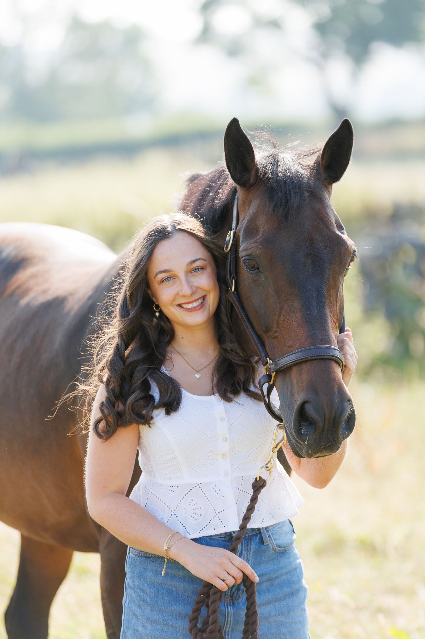 A smiling couple stands with a black and white horse and small dog in front of a white van on a farm.