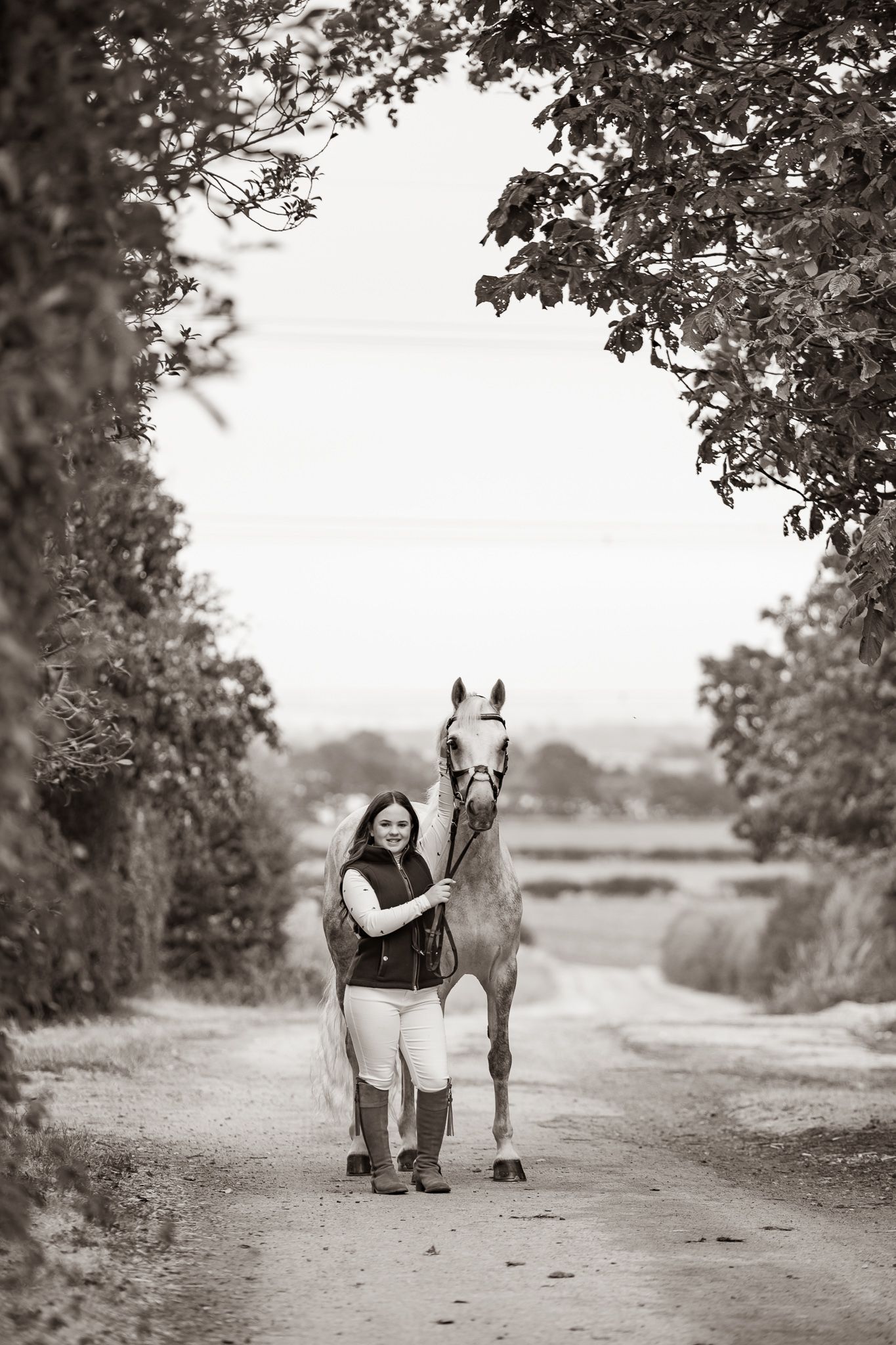 A smiling couple stands with a black and white horse and small dog in front of a white van on a farm.