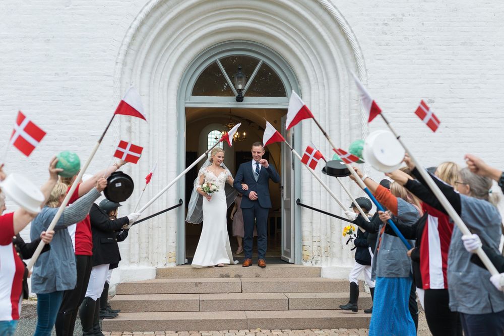 Brudepar kommer ud af kirken mellem flagsvængende gæster – bryllupsfoto af Martin & Louise