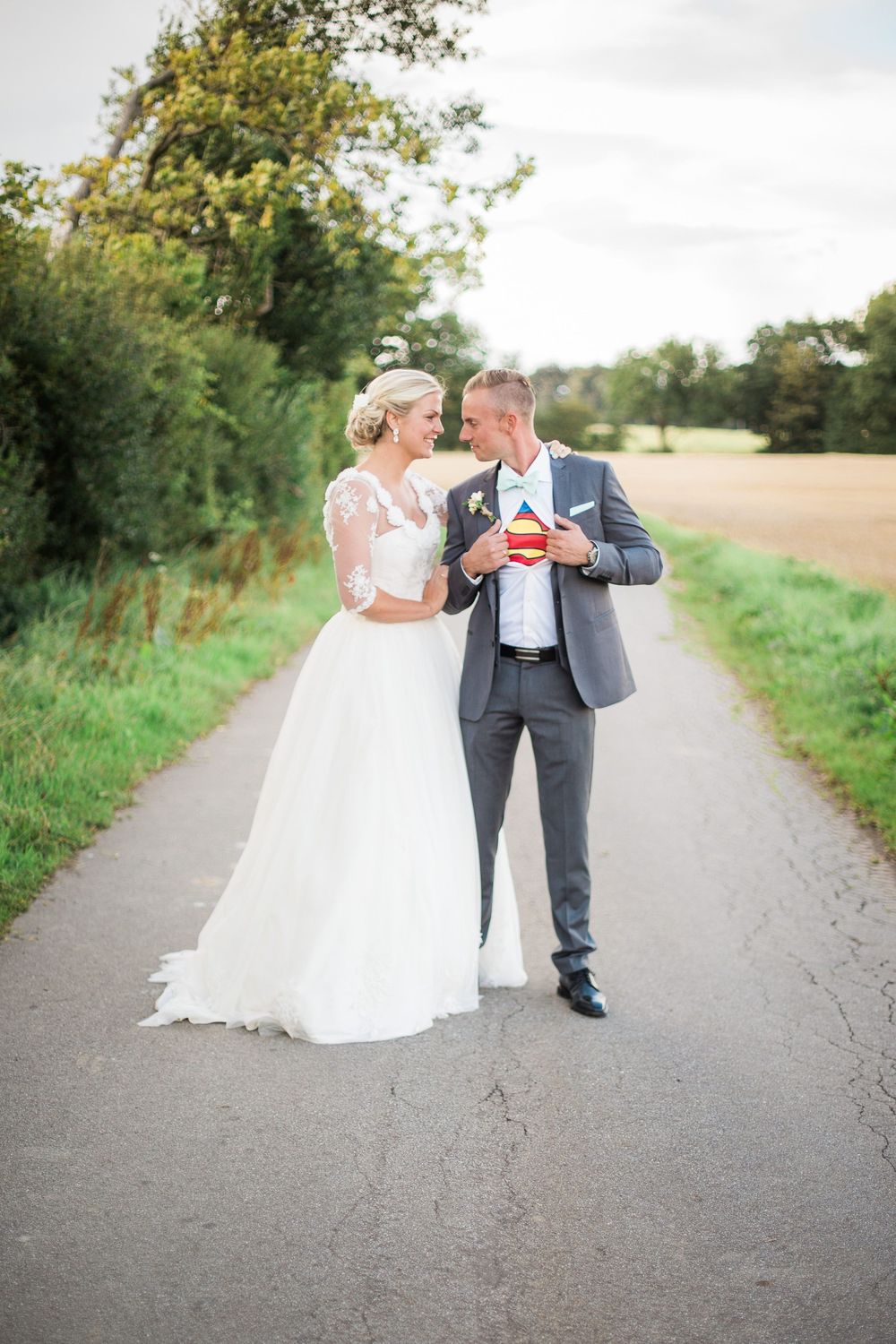 Brudepar går på landevej mellem marker – bryllupsfoto af Martin & Louise