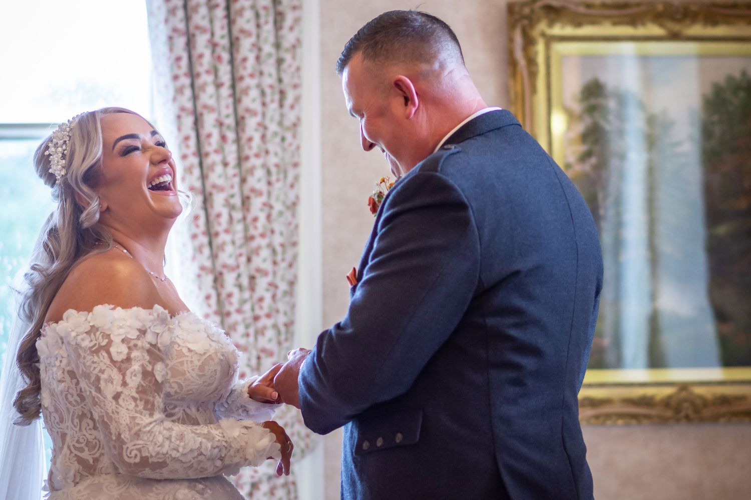 A joyful bride in lace gown laughs with groom in navy suit during wedding ceremony exchanging of the rings at Runcorn Town Hall