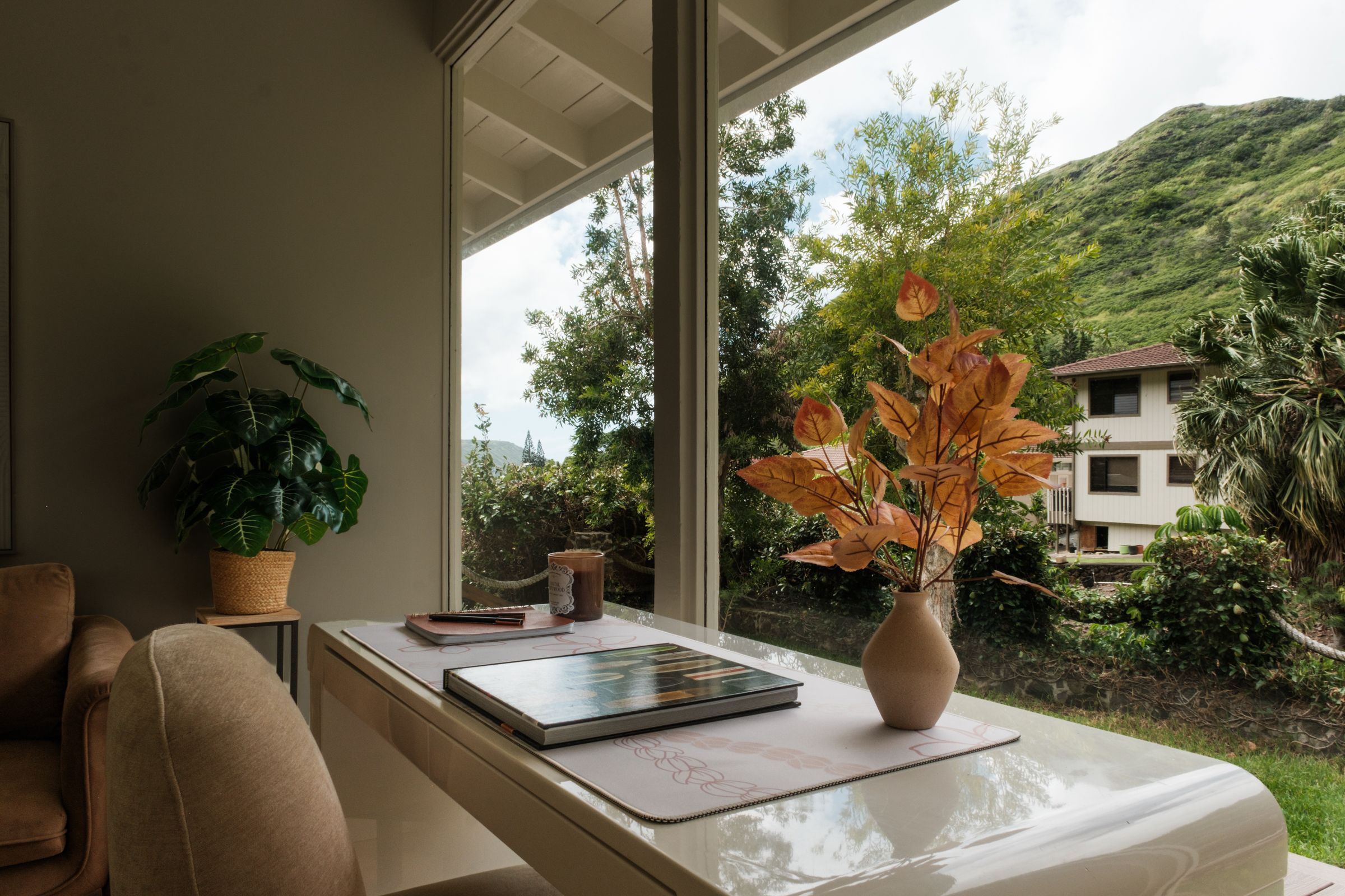 Desk with an orange floral arrangement beside large windows overlooking tropical greenery.