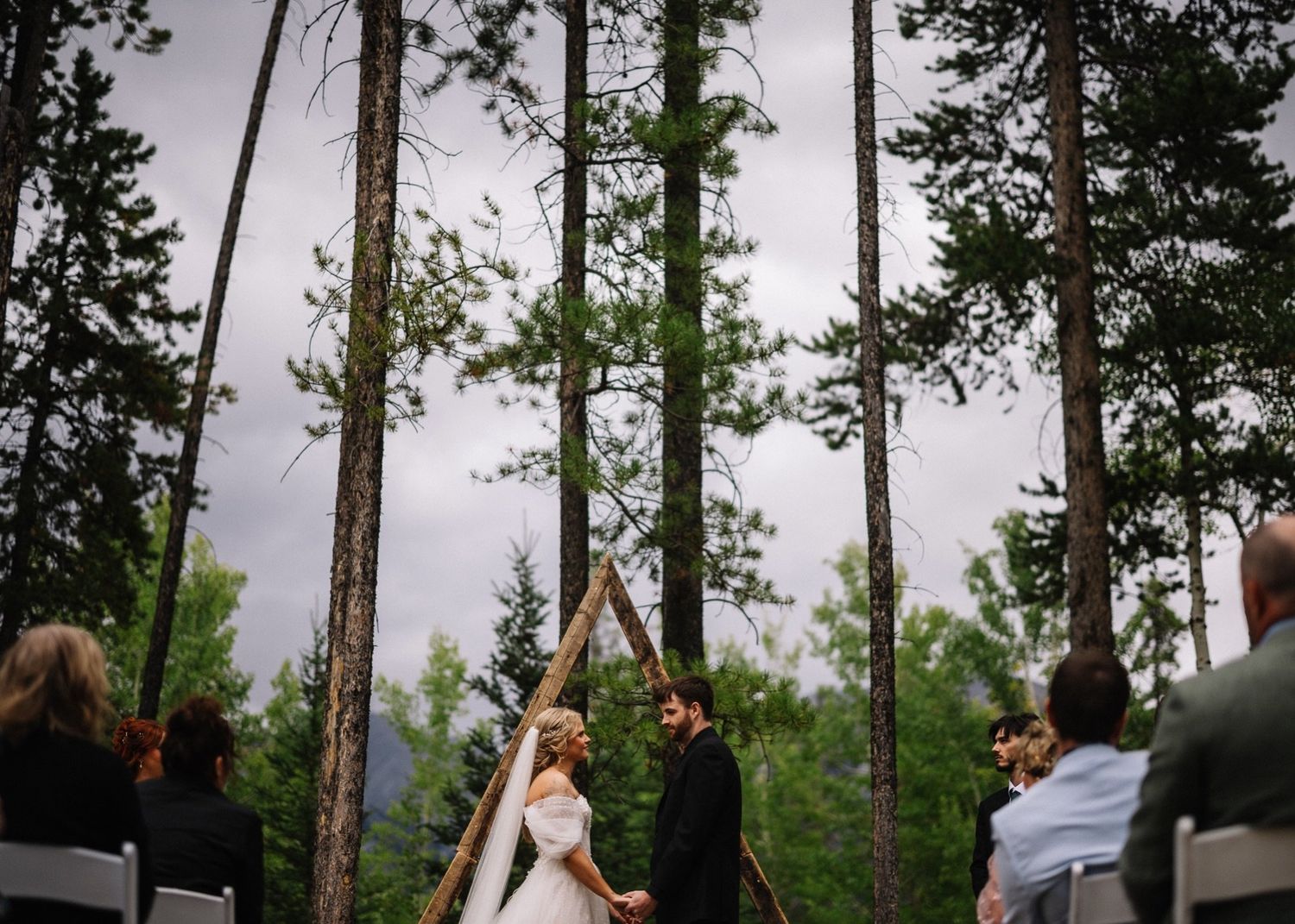 Tree Island wedding ceremony at the Canmore Nordic Centre, couple at a wooden A-frame arch among tall pines