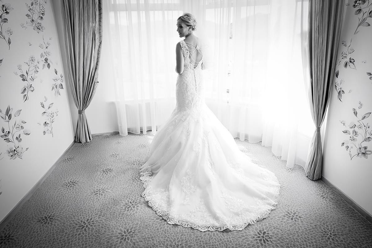 Black and white bridal portrait beside a curtained window in the bridal suite at the Inn on the Lake
