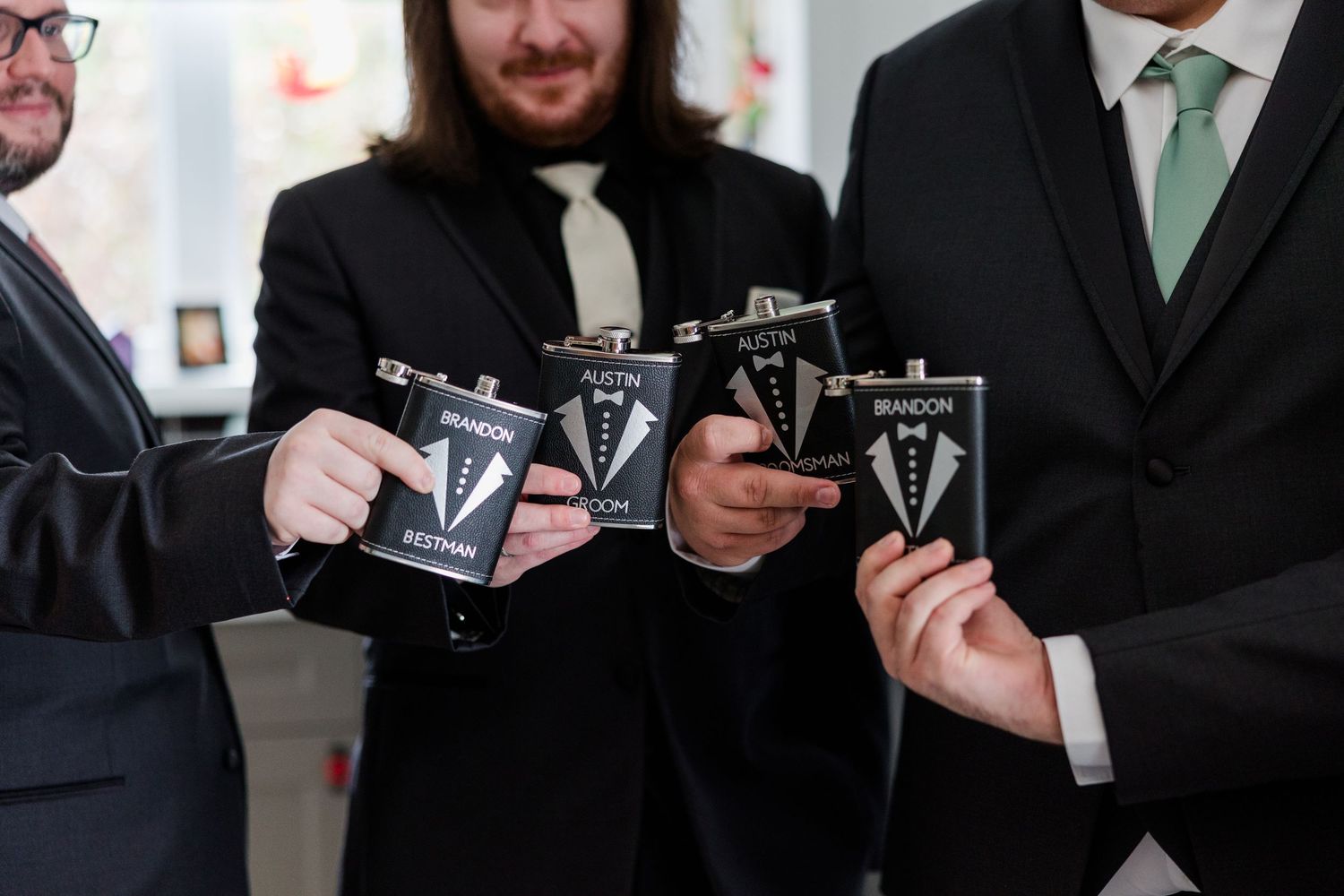 Groomsmen holding personalized black tuxedo flask gifts at a wedding celebration.