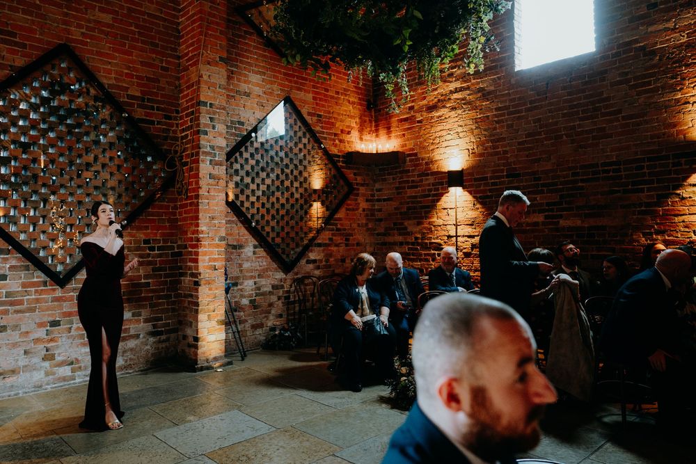 Elegant singer in black gown performing at rustic brick wedding venue with decorative diamond windows.
