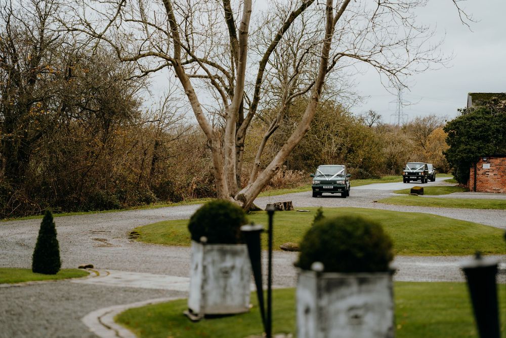 Tree-lined driveway of a countryside wedding venue with cars arriving on an overcast autumn day.