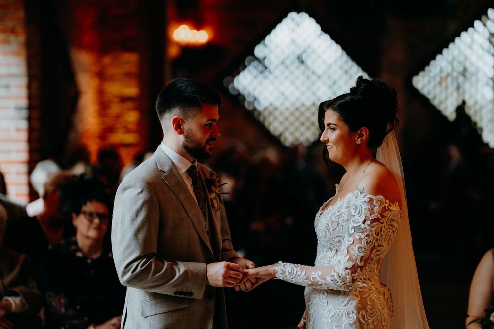Bride in lace off-shoulder gown and groom in grey suit holding hands during intimate wedding ceremony.