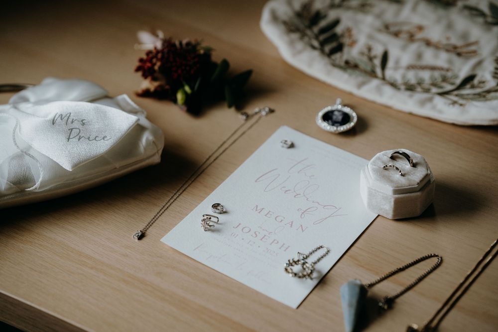 Flat lay of elegant wedding stationery, rings, earrings and accessories for Megan and Joseph.
