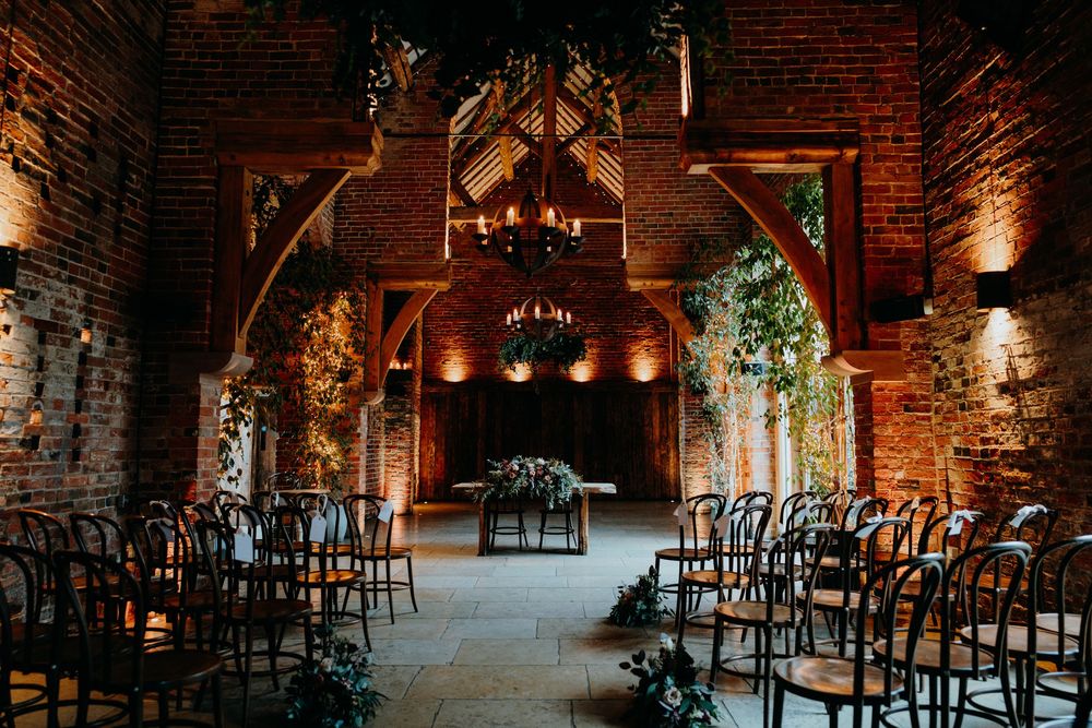 Elegant rustic barn wedding ceremony setup with brick walls, chandeliers and floral arch.